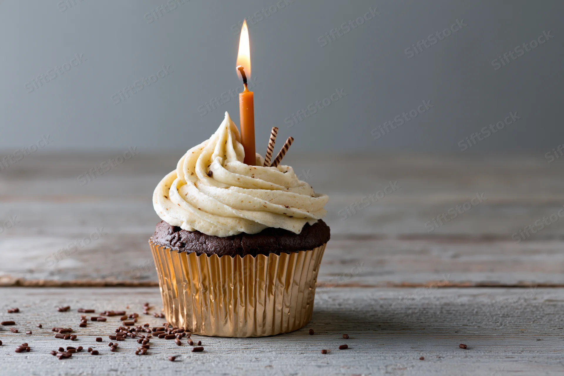 Chocolate cupcake with lit candle and cream frosting on wooden surface