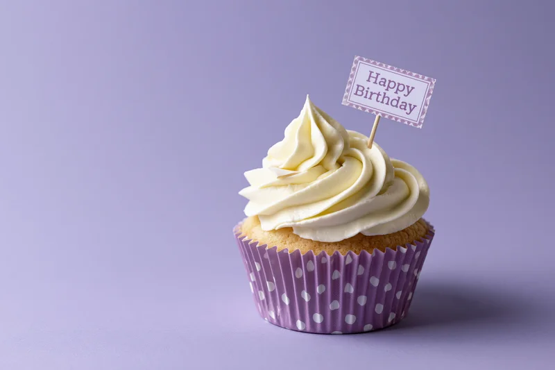 Single cupcake with white frosting and happy birthday topper on purple background