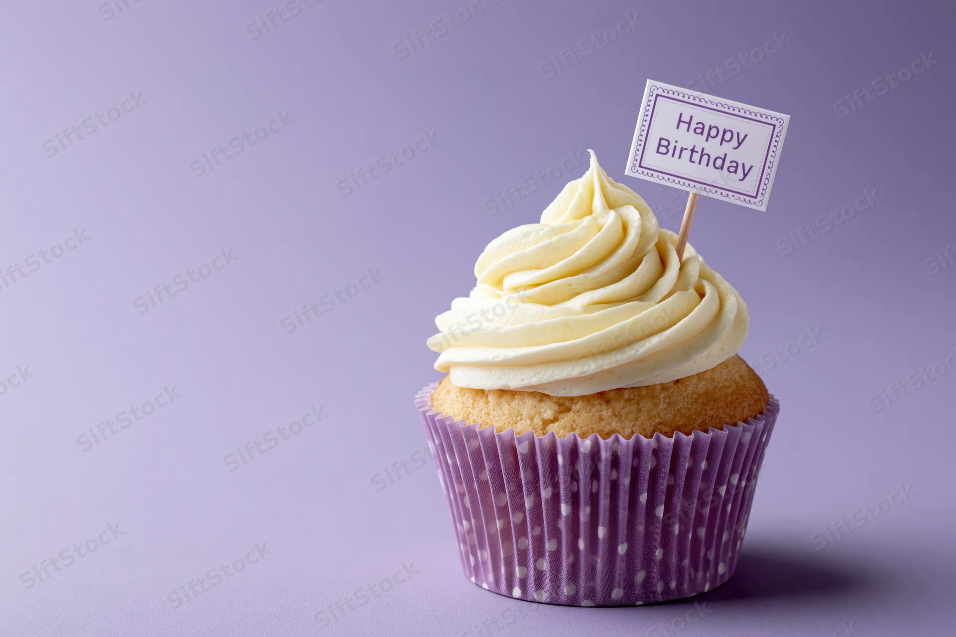 Single cupcake with white frosting and happy birthday sign in purple polka dot liner on lavender background