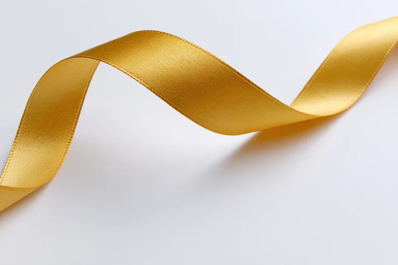 Gold satin ribbon twisting diagonally across white background