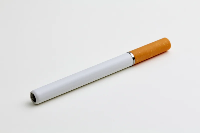 Electronic cigarette with white body and orange filter lying on white surface