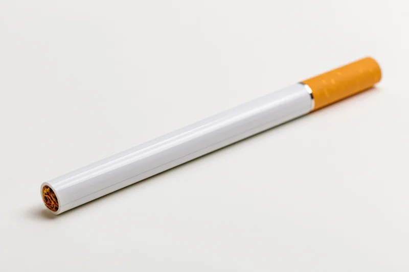 Electronic cigarette with white body and orange tip lying on white surface