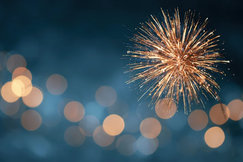 Golden firework bursting in night sky with bokeh lights in background