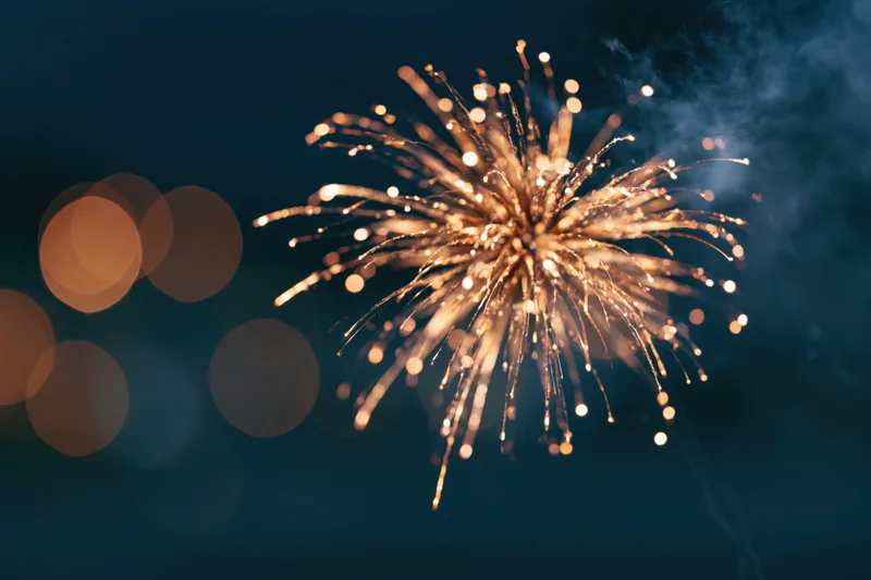 Golden firework burst exploding in the night sky with bokeh lights in the background