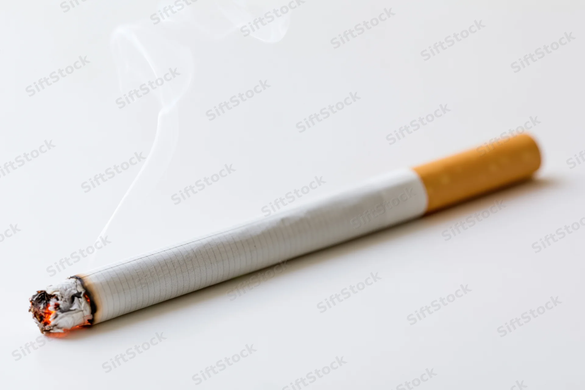 Lit cigarette with smoke rising from burning end on white surface