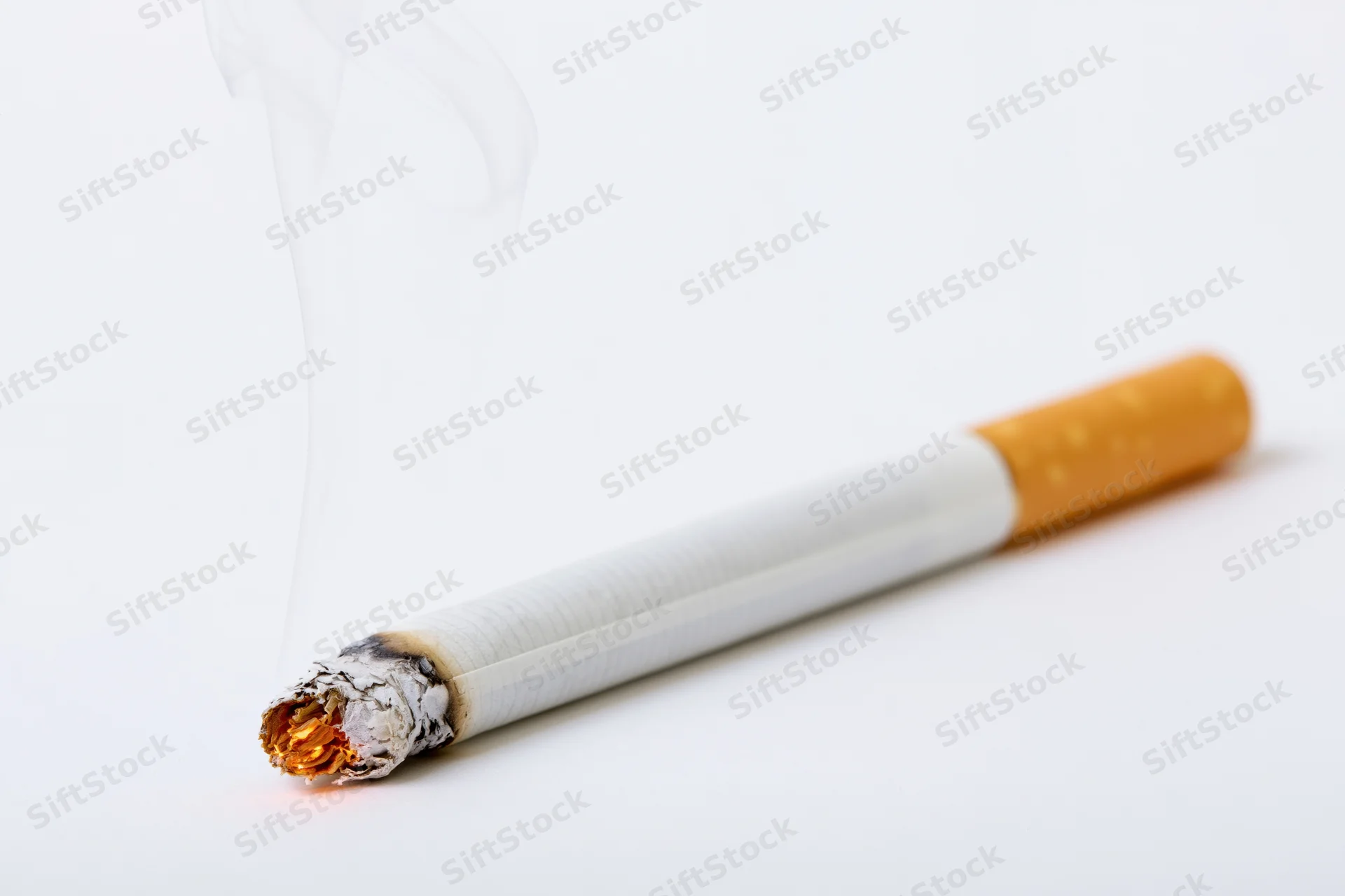 Lit cigarette with smoke and ash resting horizontally on white surface