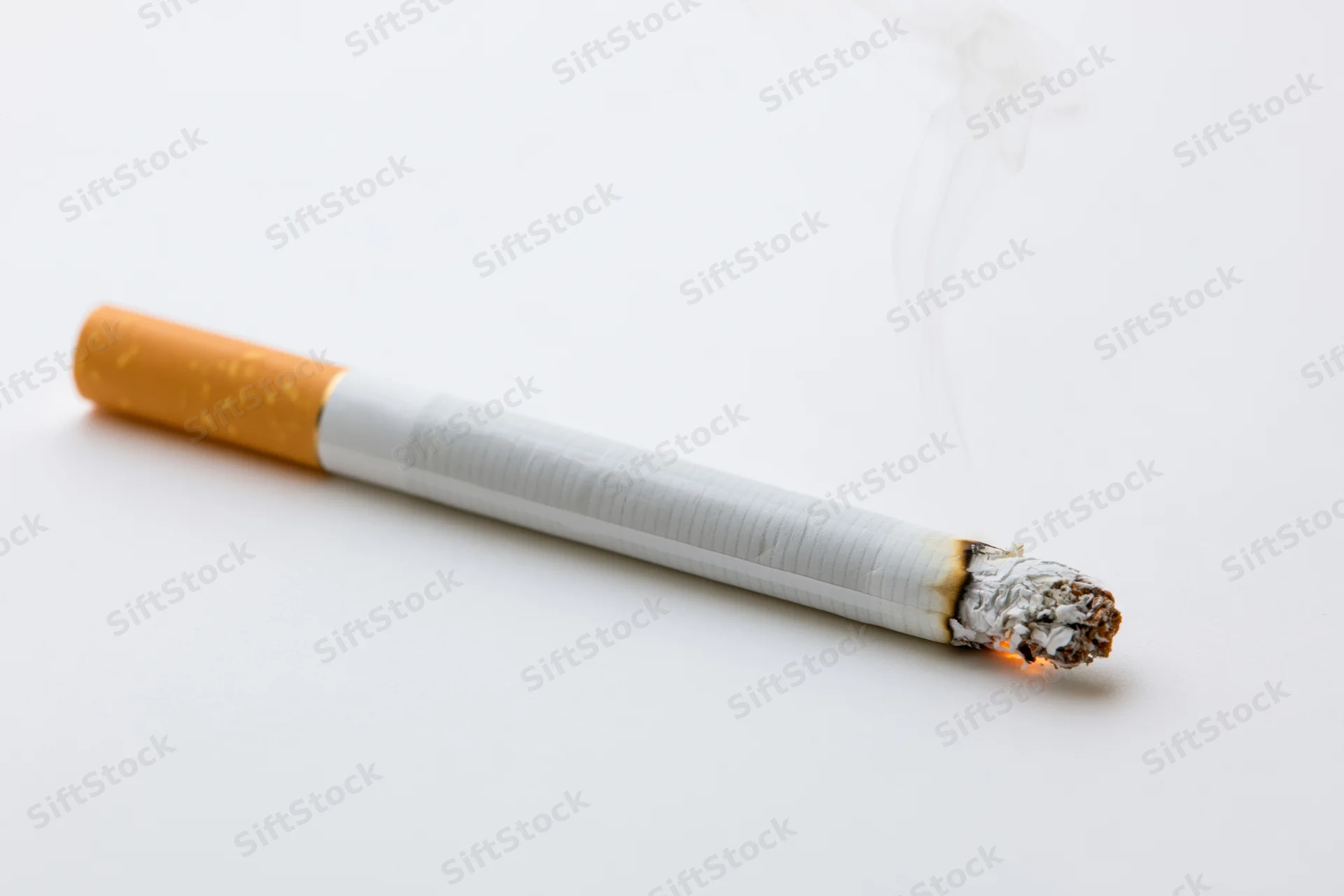 Lit cigarette with white smoke and ash resting horizontally on white surface
