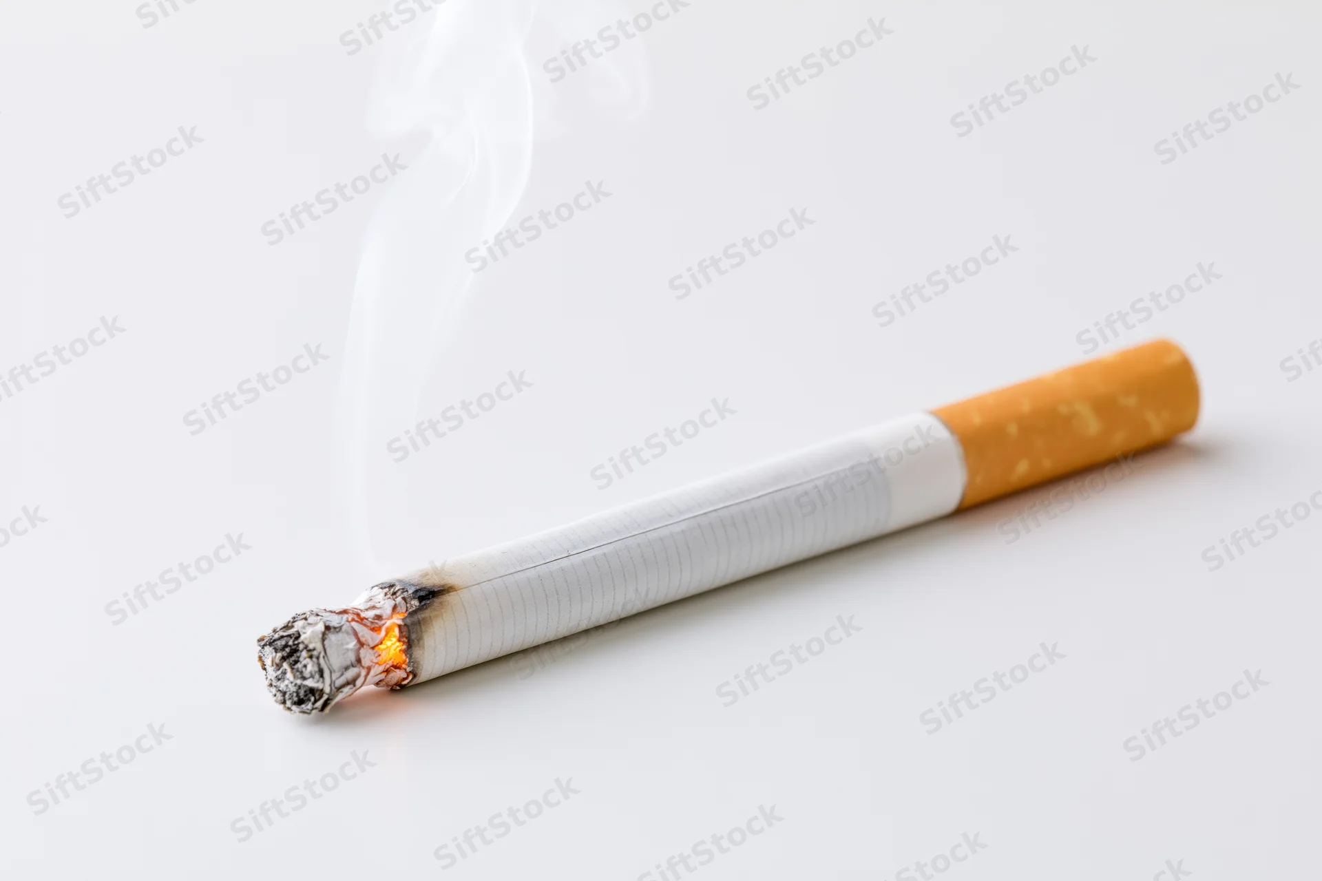 Lit cigarette burning horizontally on white background with thin smoke rising