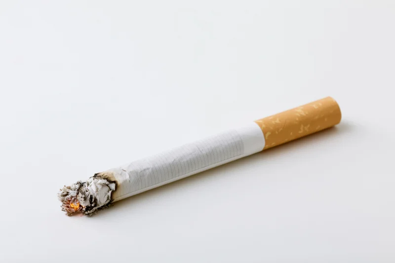 Lit cigarette with glowing ember and ash on white background