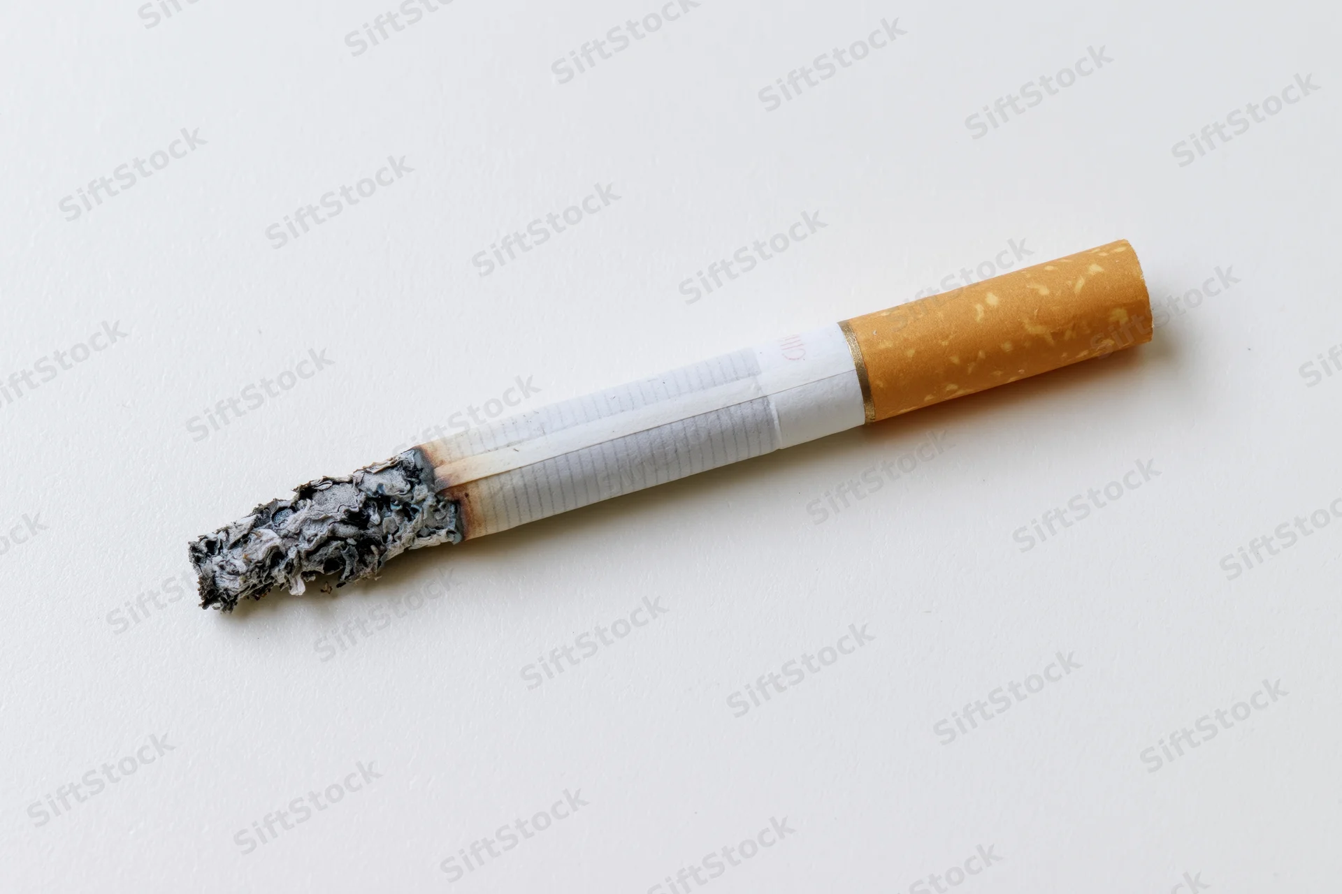 Lit cigarette with ash resting on plain white surface