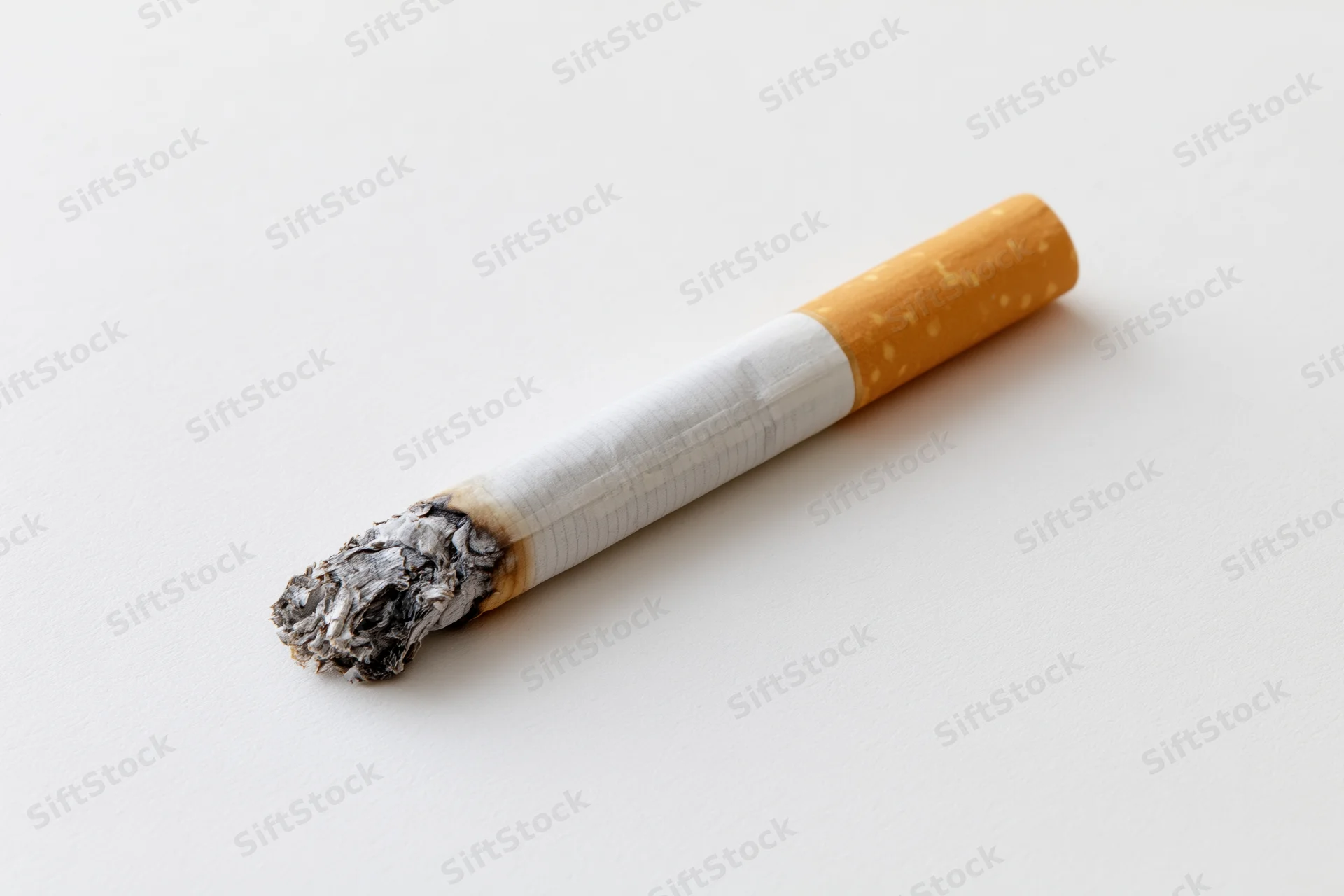 Lit cigarette with ash tip resting on plain white surface