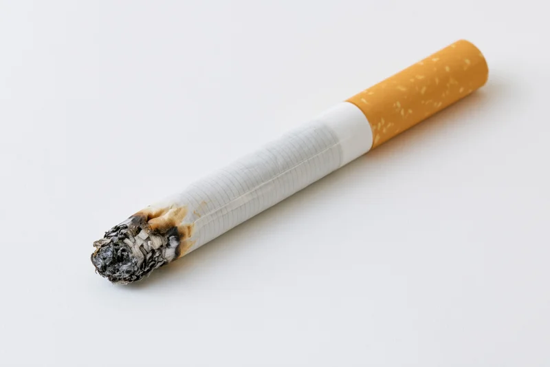 Lit cigarette with ash tip resting on plain white surface