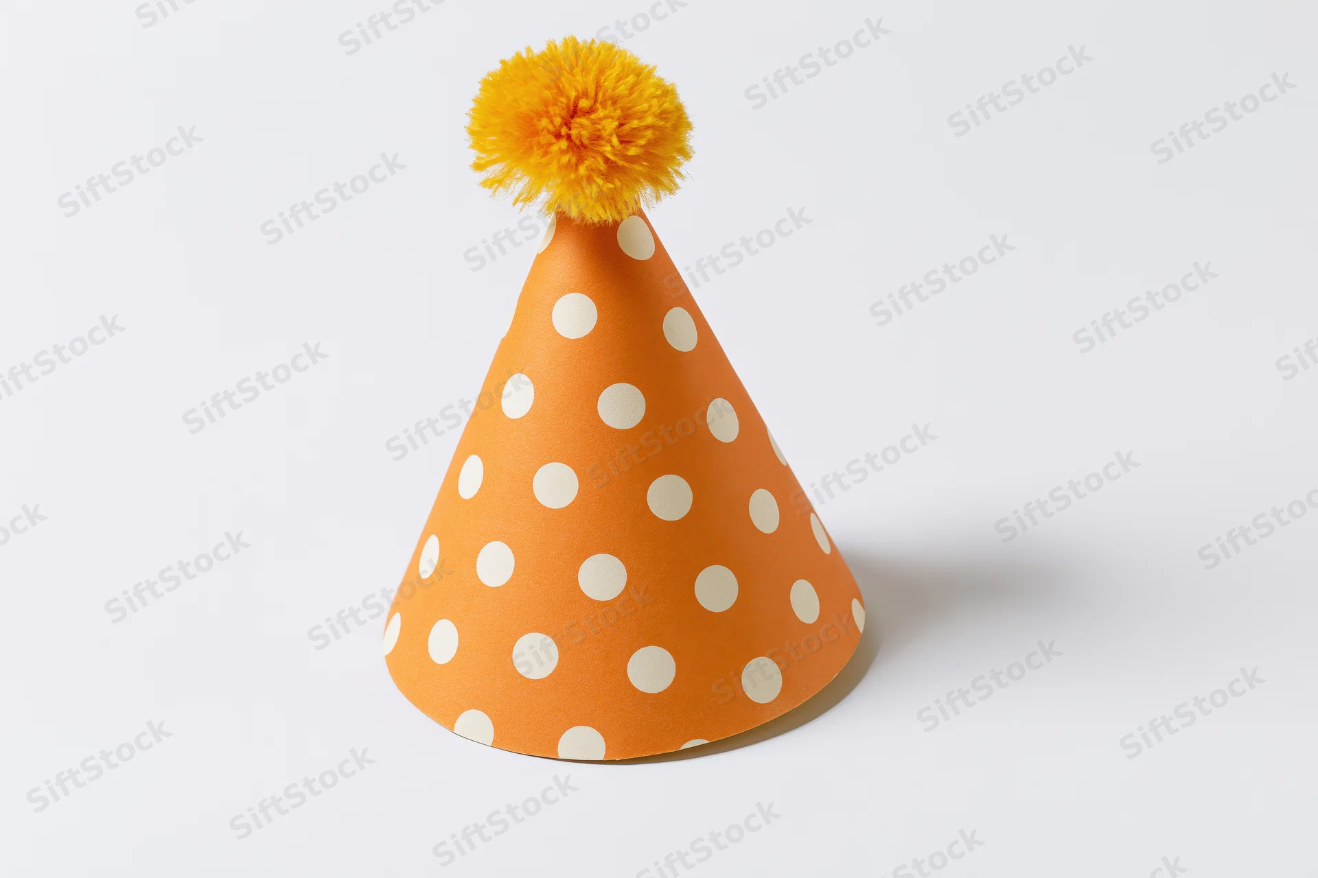 Orange polka dot party hat with yellow pompon on white background