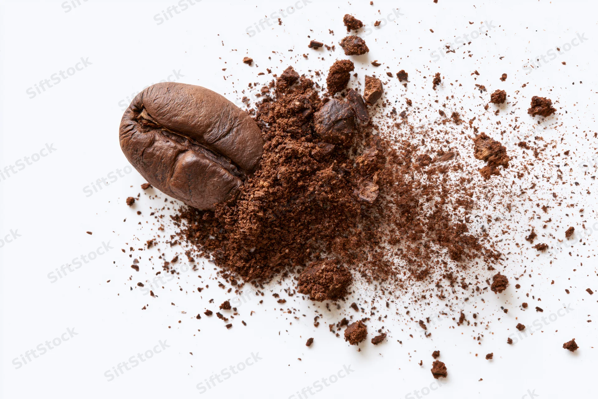 Roasted coffee bean with scattered ground coffee on white surface