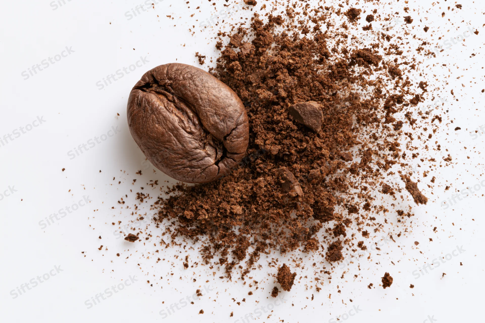 Roasted coffee bean next to a pile of ground coffee on white surface