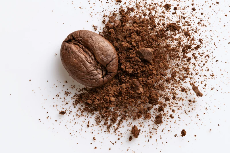 Roasted coffee bean next to a pile of ground coffee on white surface