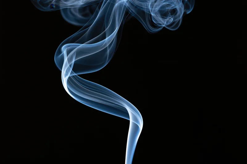 Thin ribbon of incense smoke curling and twisting upward against black background