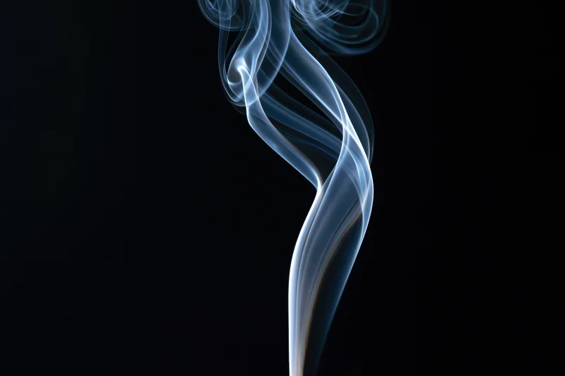 Thin ribbon of incense smoke curling and twisting upward against black background