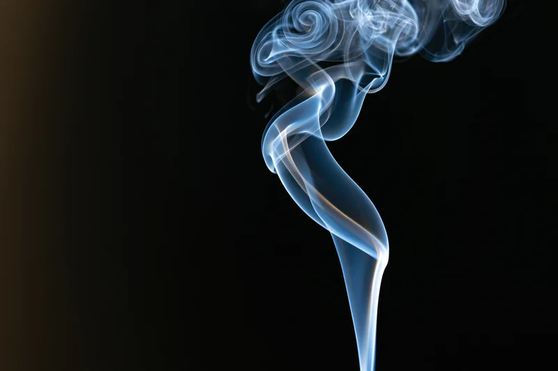Thin ribbon of incense smoke curling and twisting upward against a dark background