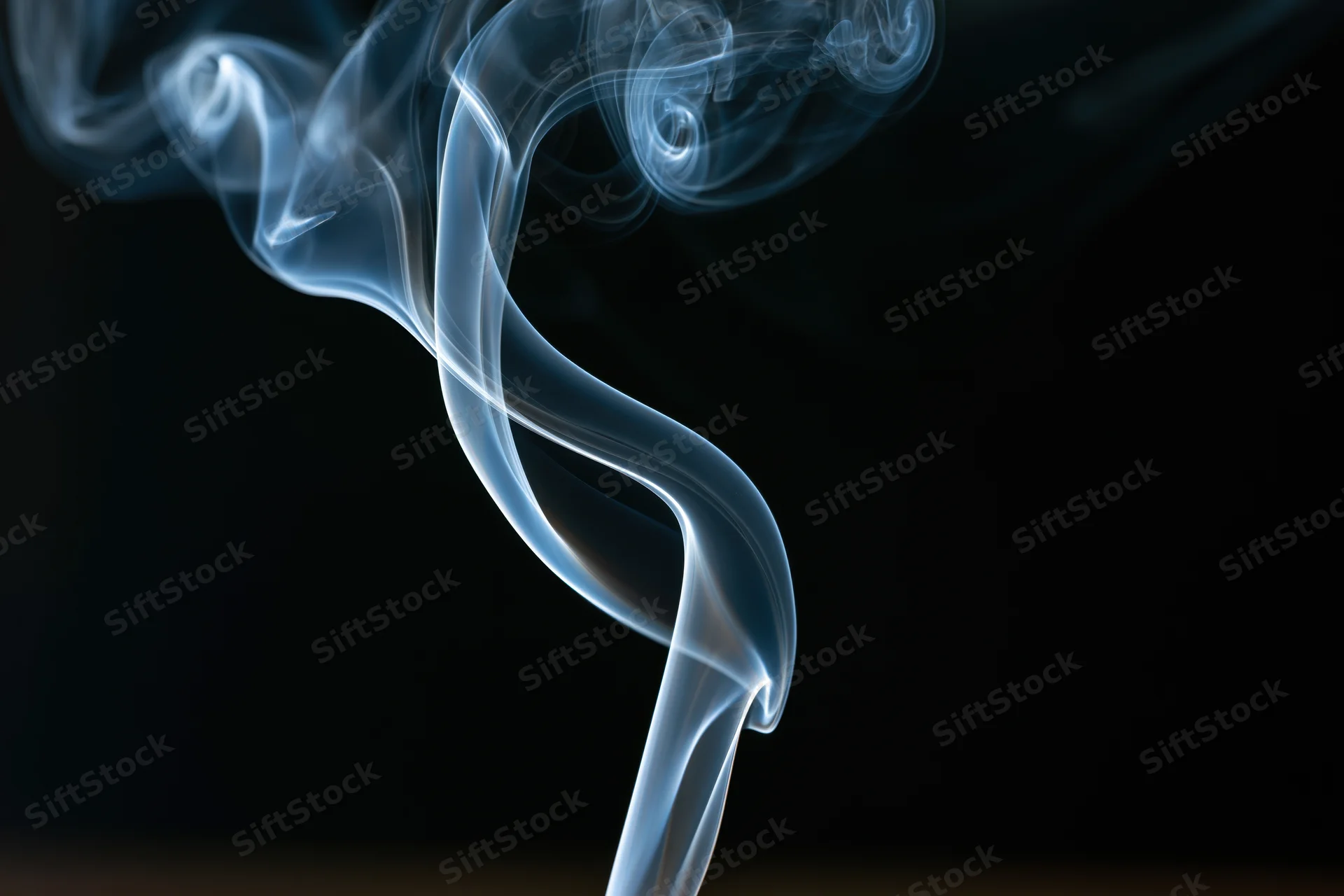 Thin ribbon of incense smoke curling and twisting upward against dark background