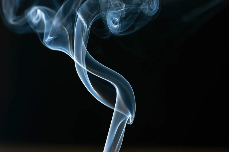Thin ribbon of incense smoke curling and twisting upward against dark background