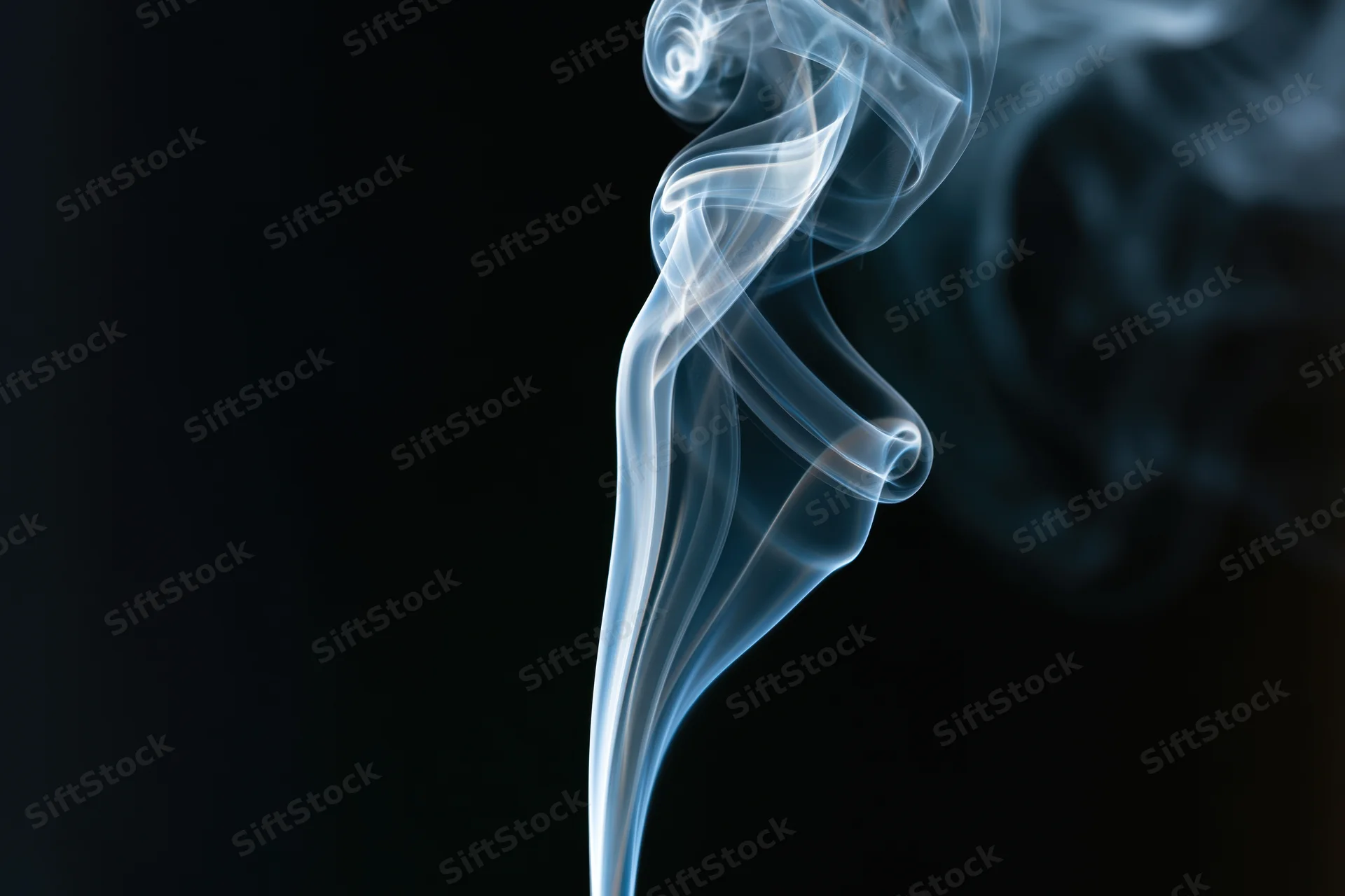 Thin wisp of smoke rising and curling against dark background