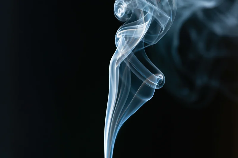 Thin wisp of smoke rising and curling against dark background