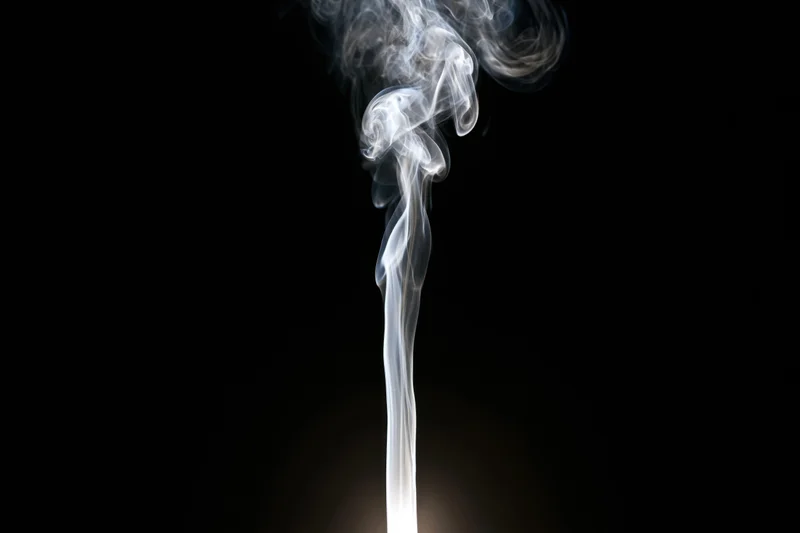 Thin wisp of white smoke rising and curling upward against black background