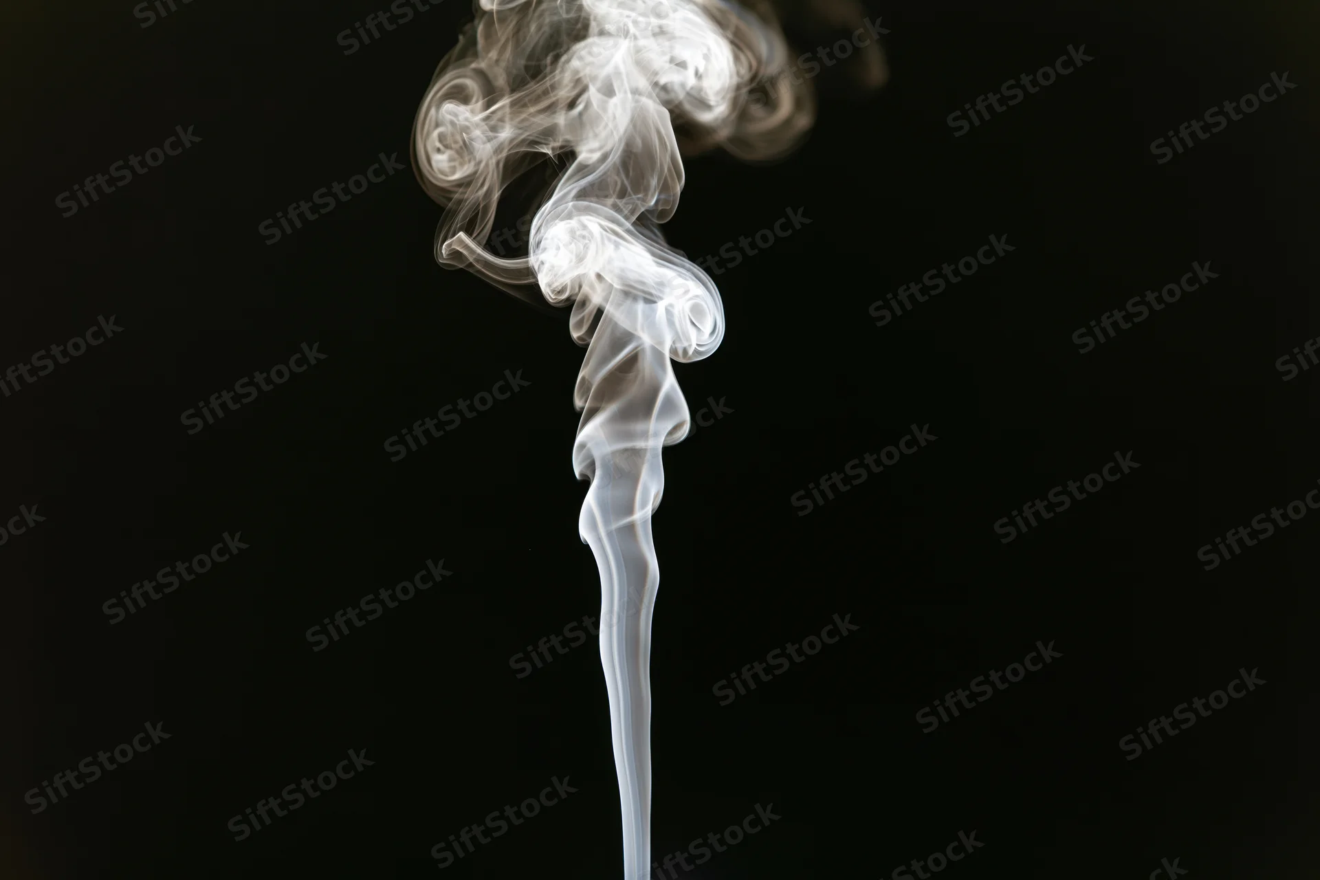 Thin wisp of white smoke rising and curling upward against black background