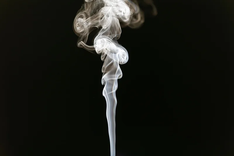 Thin wisp of white smoke rising and curling upward against black background