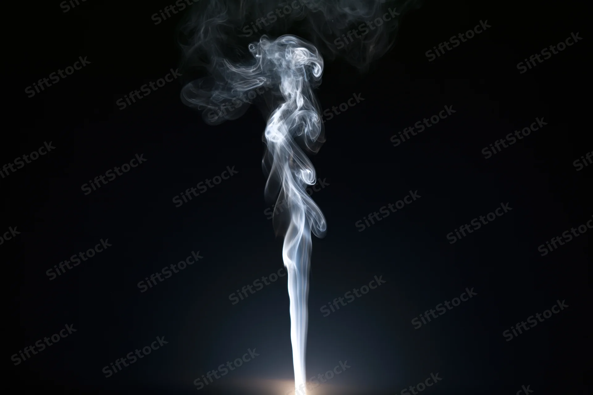 Thin wisp of white smoke rising and curling upward against black background