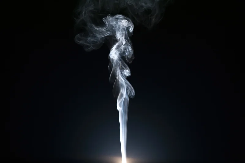 Thin wisp of white smoke rising and curling upward against black background