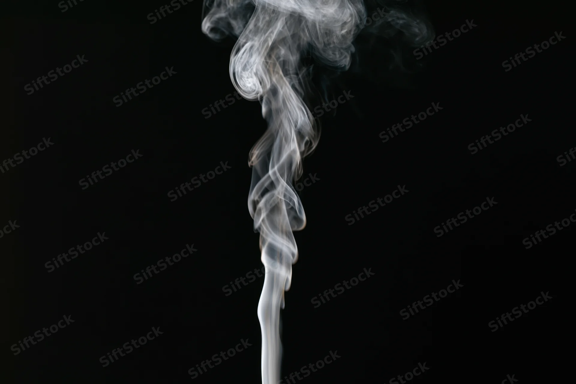 Thin wisp of white smoke rising and curling upward against black background