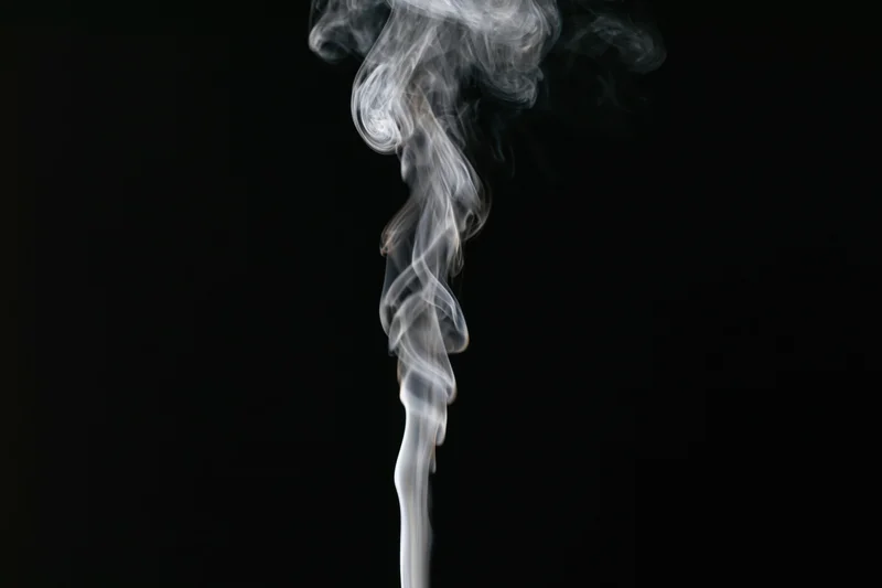 Thin wisp of white smoke rising and curling upward against black background