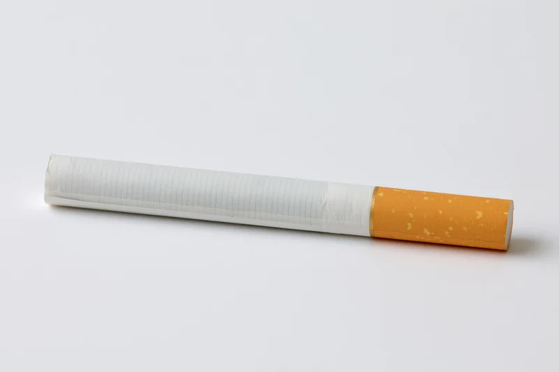 Unlit cigarette lying horizontally on plain white surface