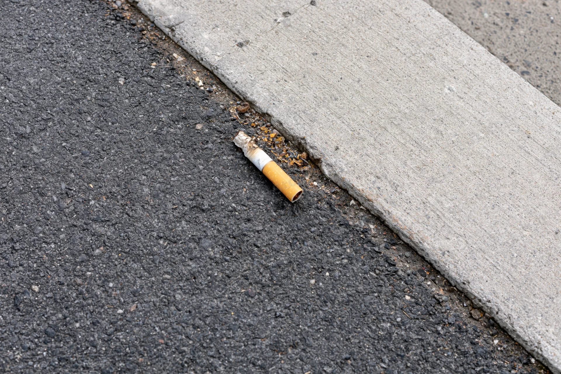 Used cigarette butt lying on the boundary between asphalt road and concrete sidewalk