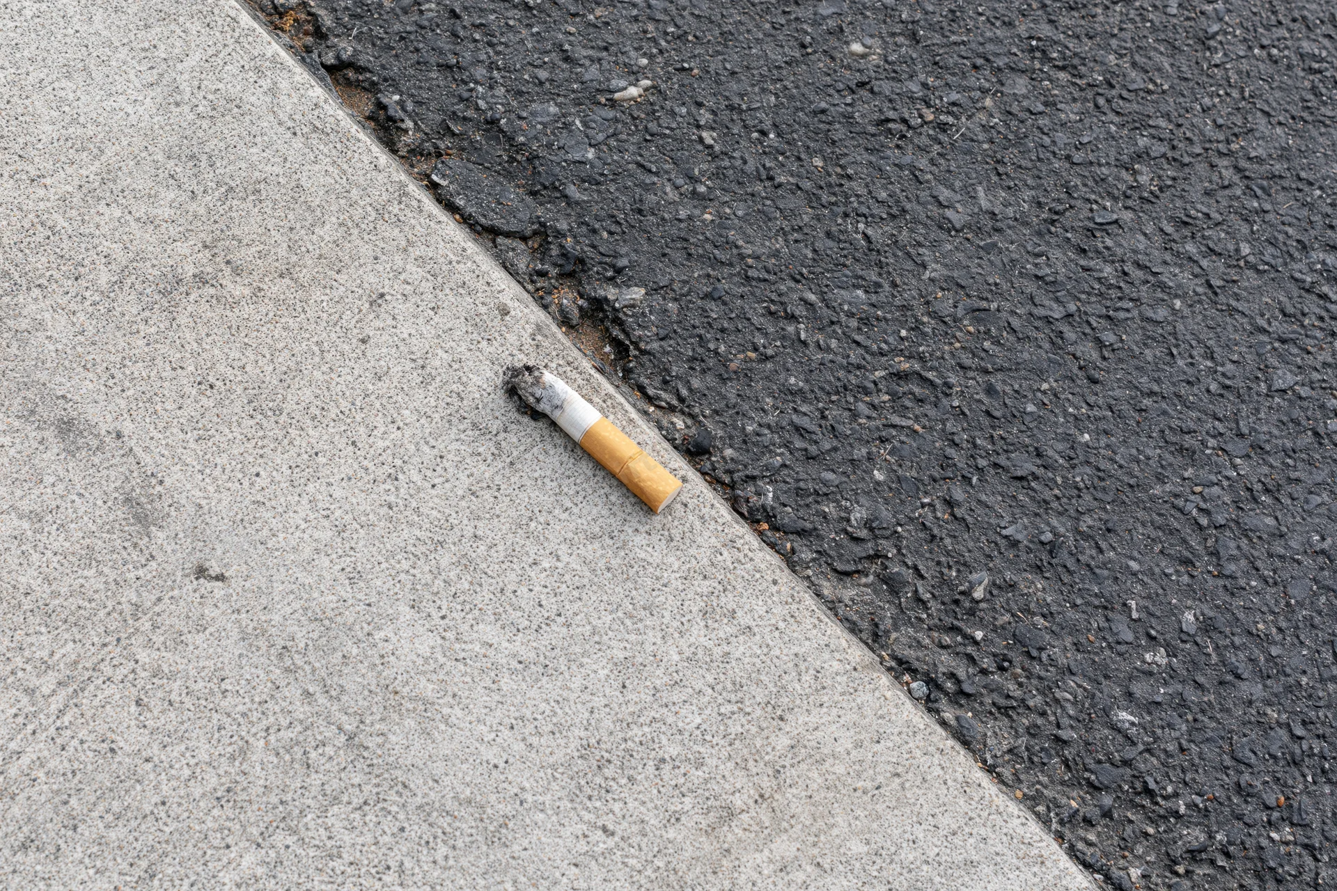 Cigarette butt lying on the boundary between pavement and asphalt street