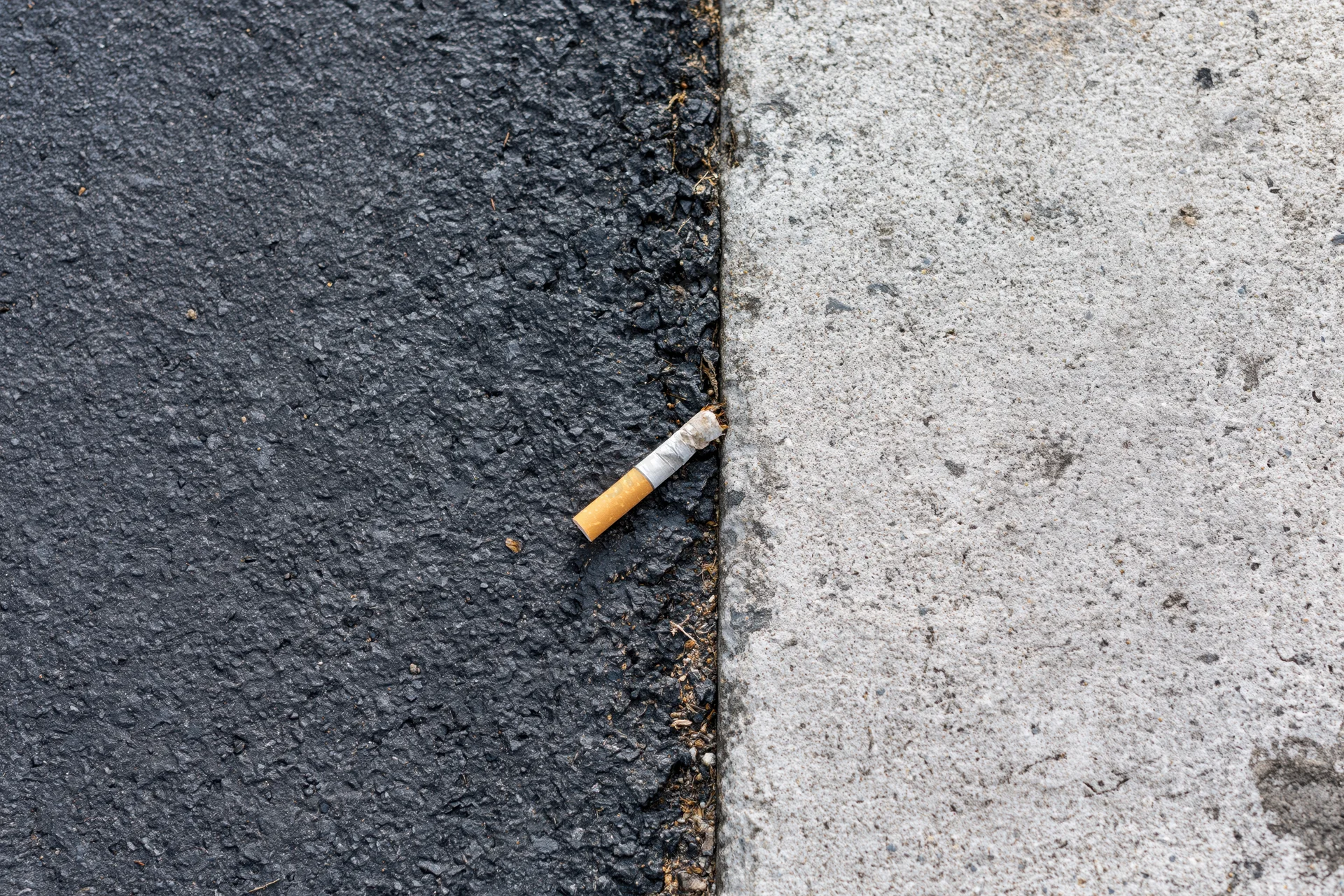 Cigarette butt lying on the boundary between asphalt and concrete pavement