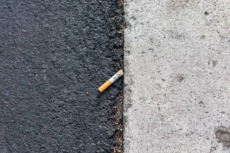 Cigarette butt lying on the boundary between asphalt and concrete pavement