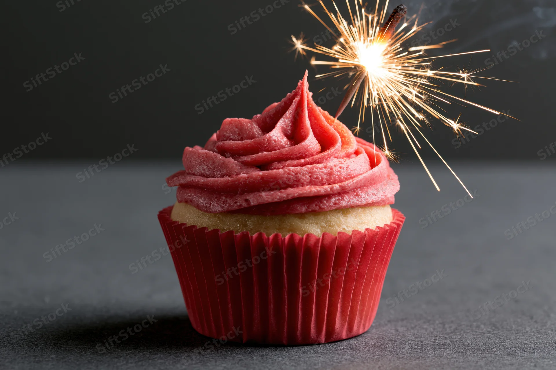 Single vanilla cupcake with red frosting and sparkler on dark surface