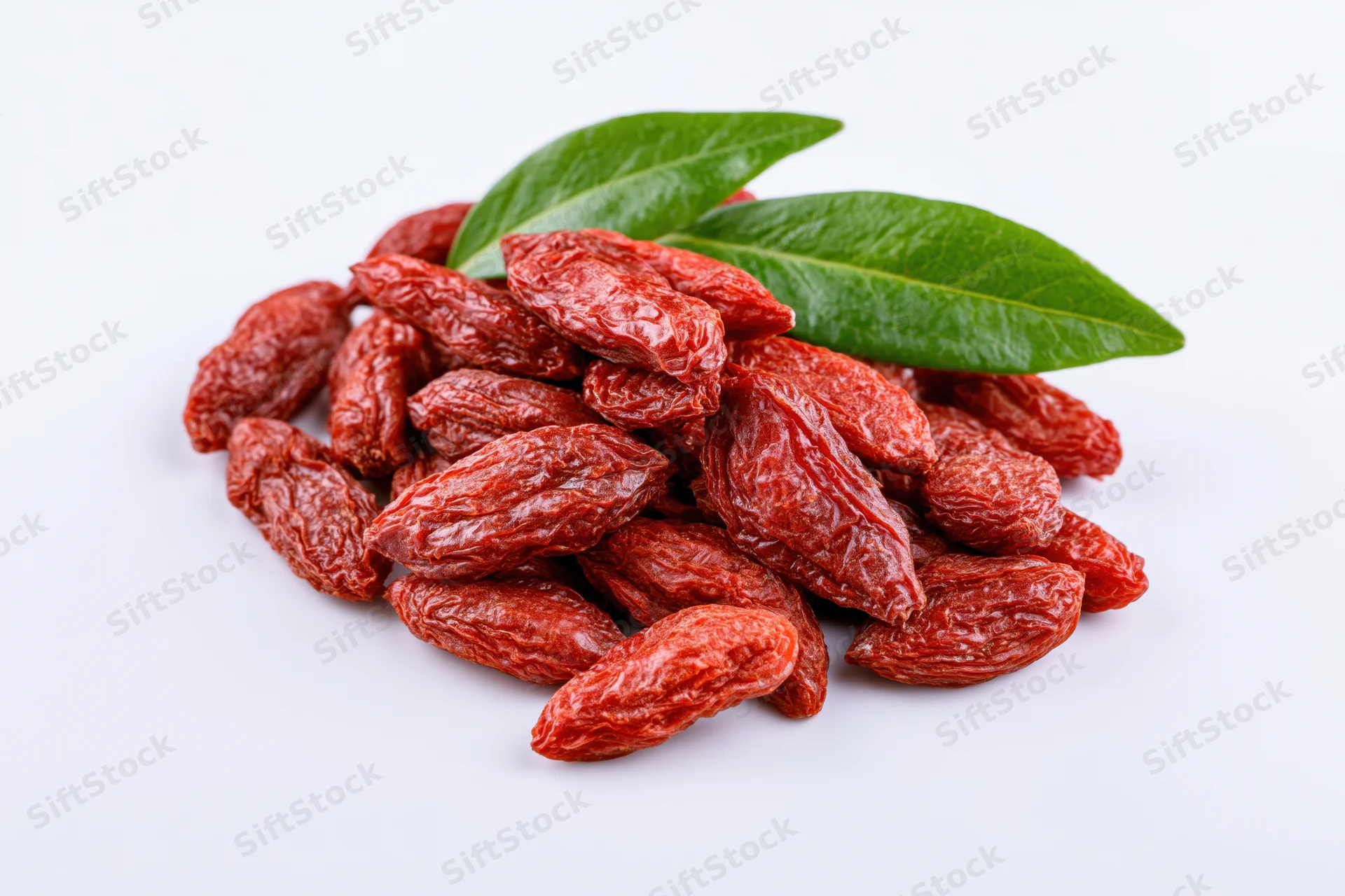Pile of dried goji berries with two green leaves on white background