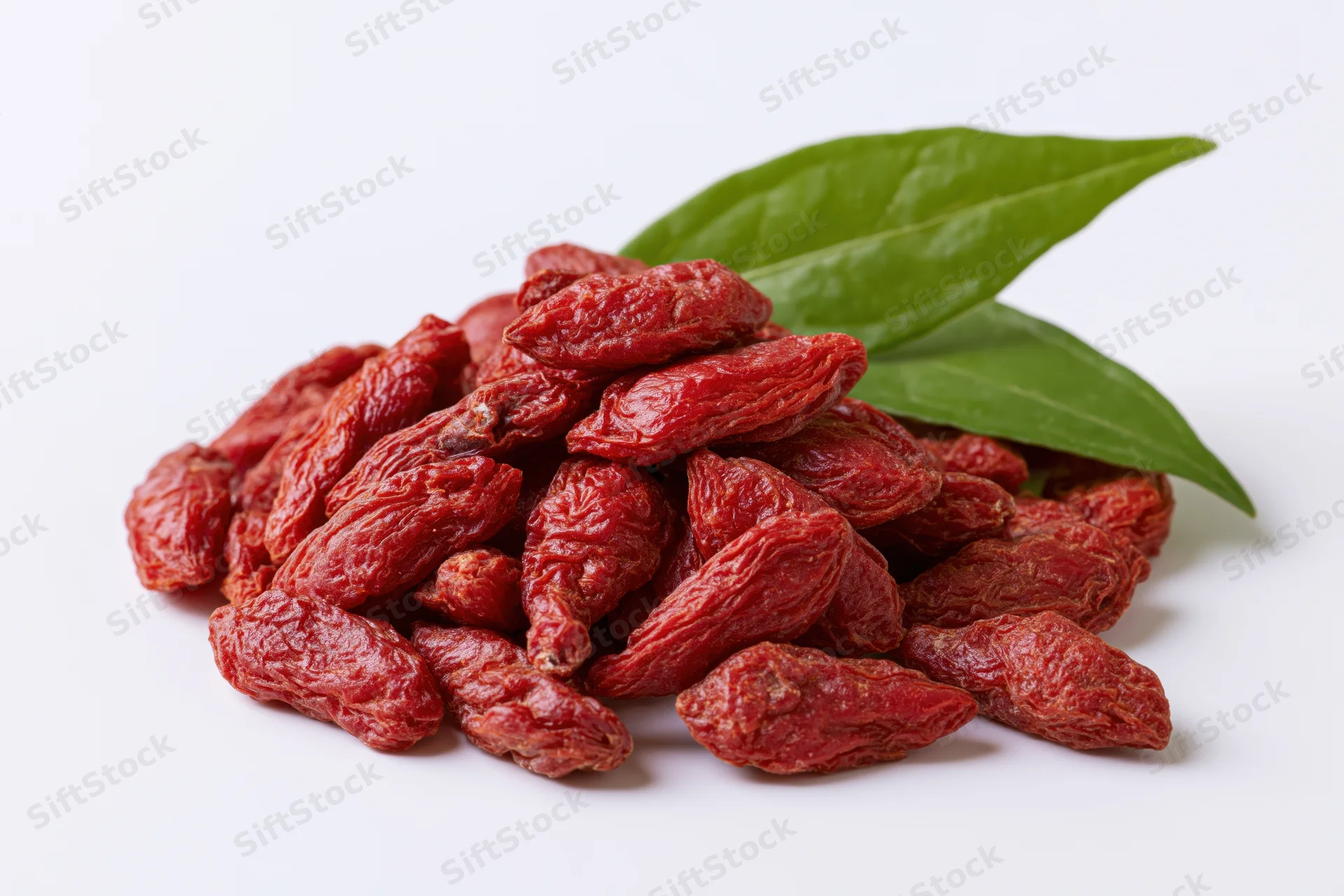 Pile of dried goji berries with two fresh green leaves on white background