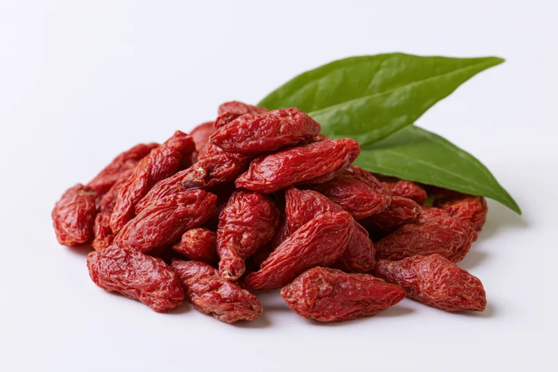 Pile of dried goji berries with two fresh green leaves on white background