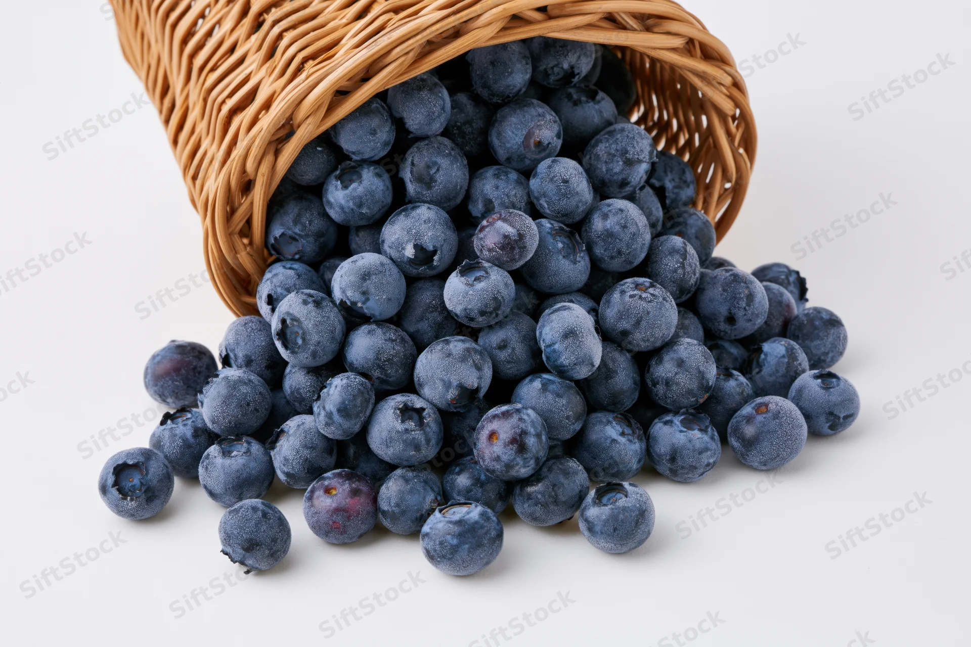 Blueberries spilling from a tipped wicker basket on white background