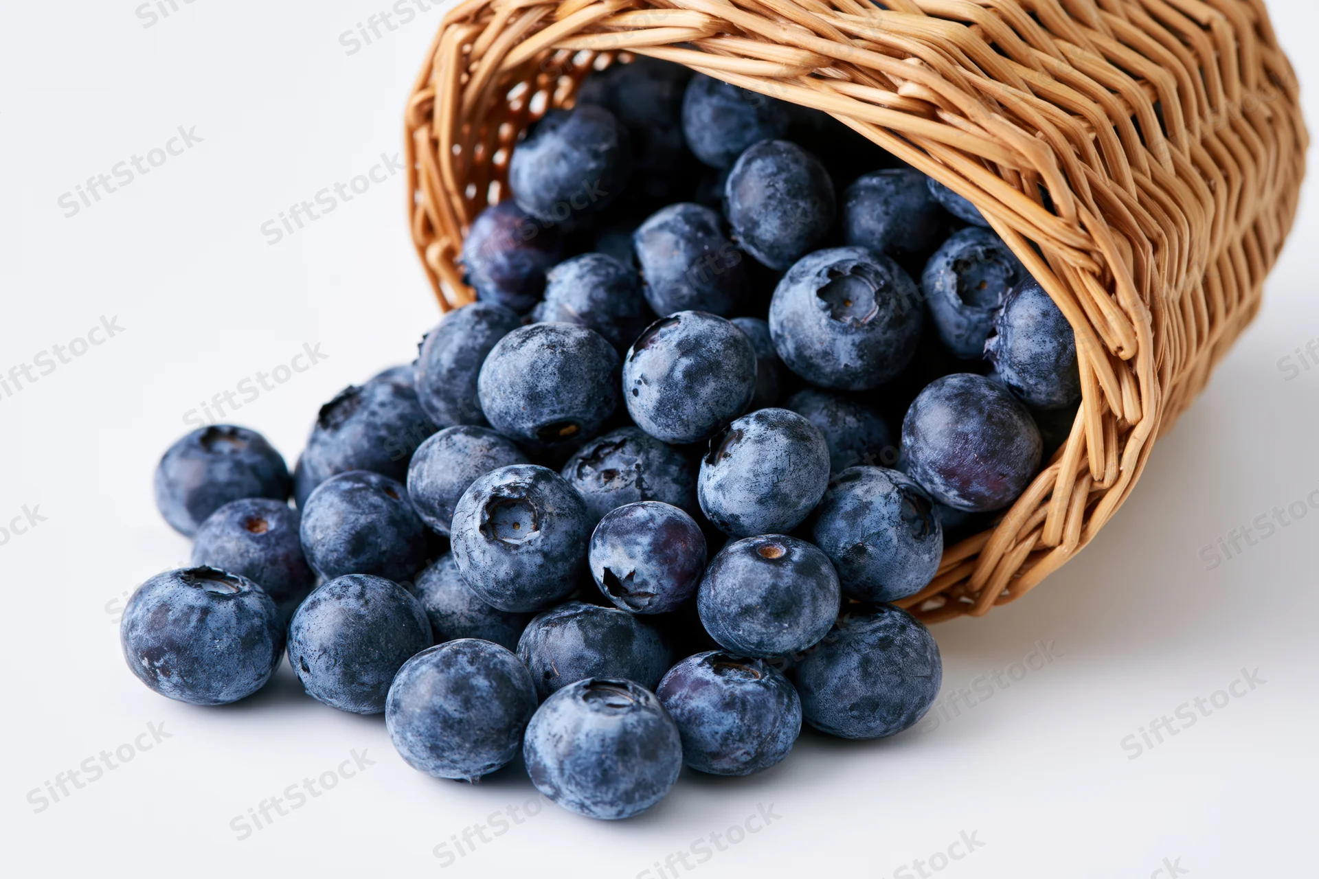 Blueberries spilling from a tipped wicker basket on white background