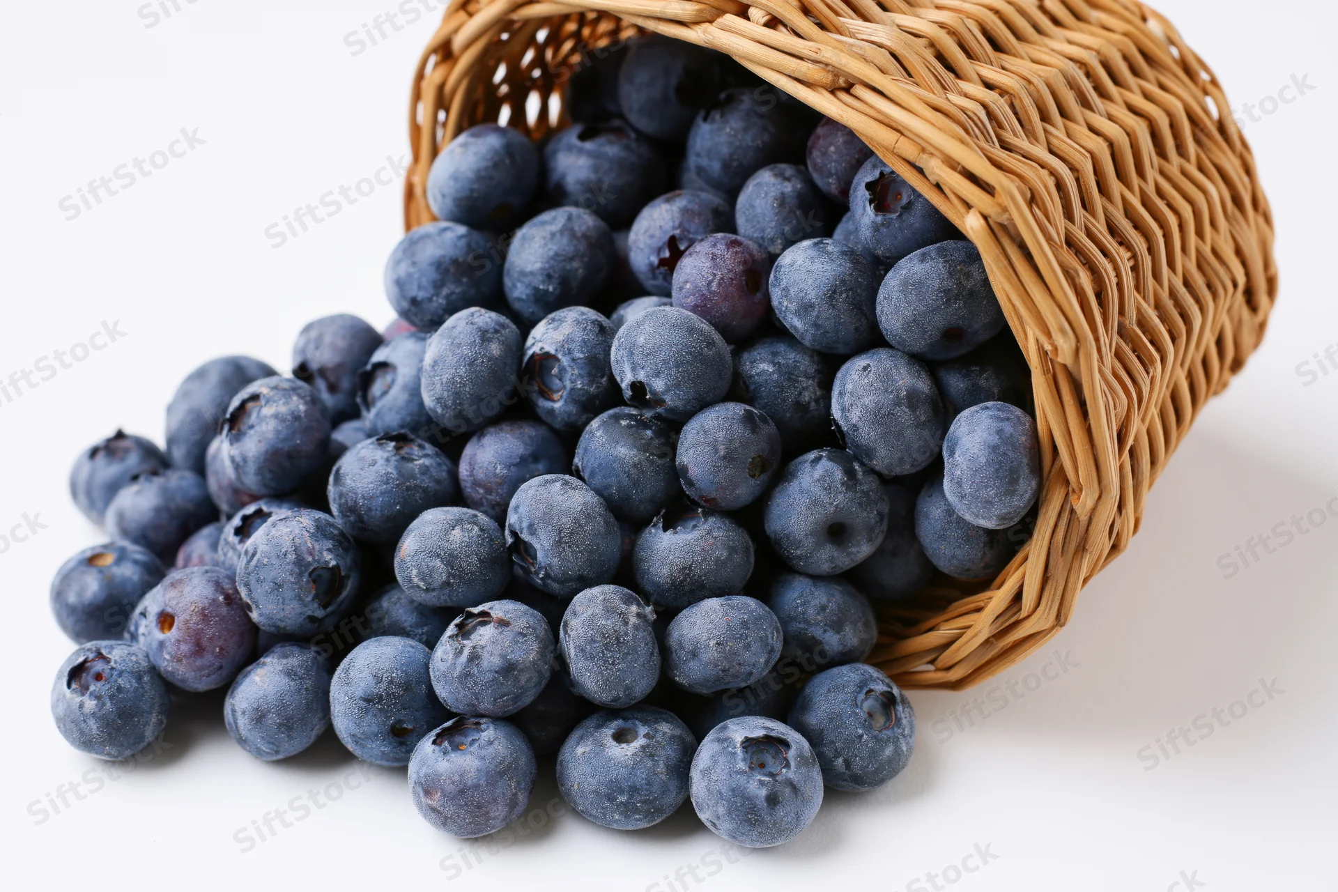Blueberries spilling from a tipped wicker basket on white background