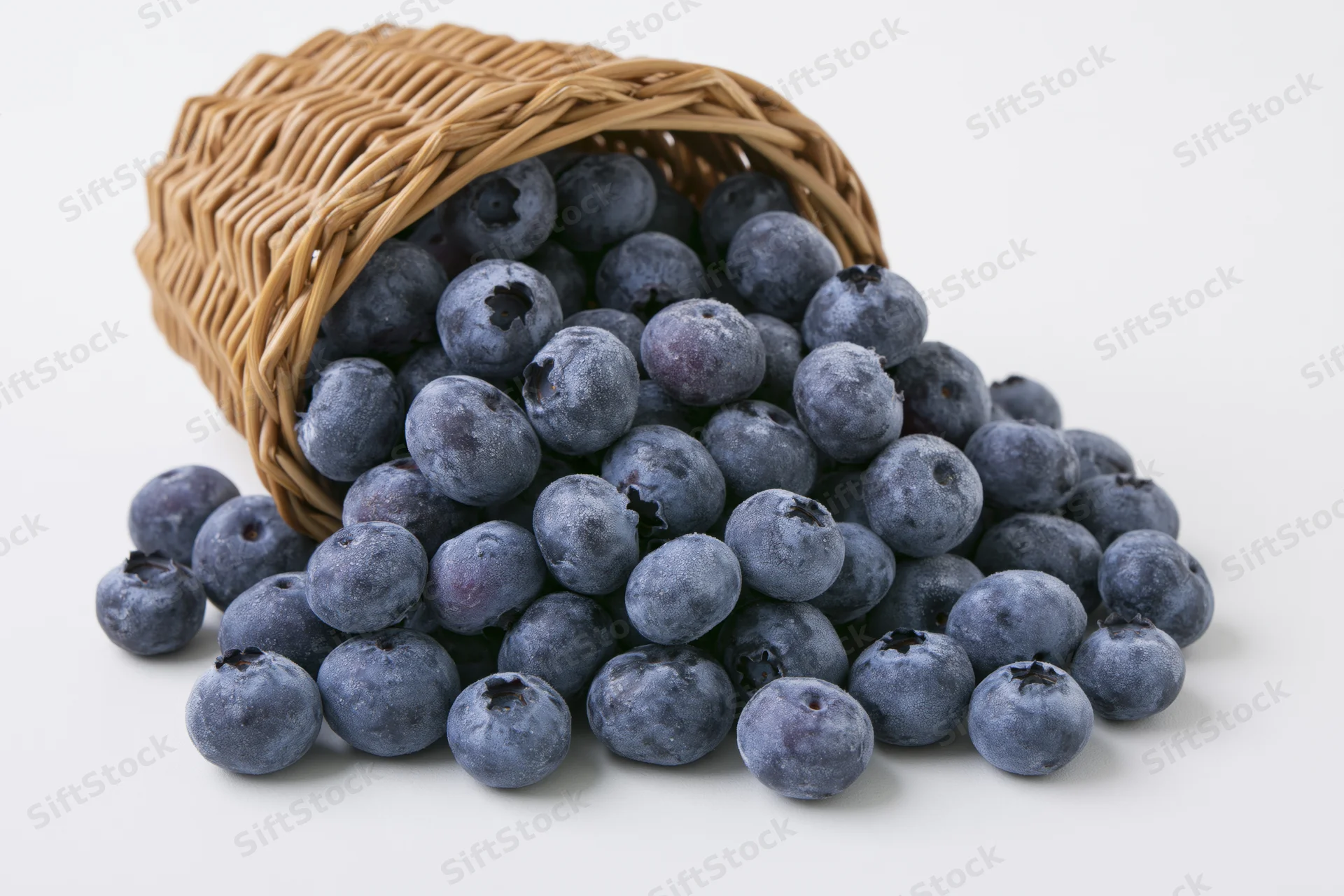 Blueberries spilling from a tipped wicker basket on white background