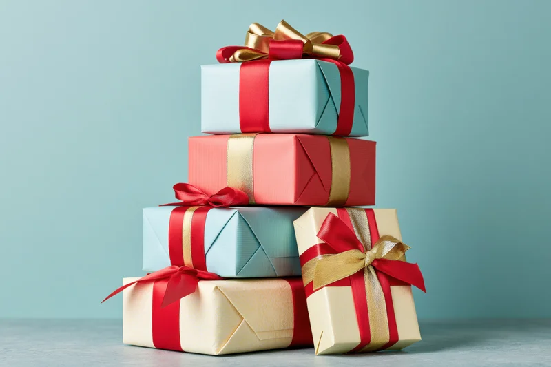 Stack of wrapped gift boxes with red and gold ribbons on a flat surface