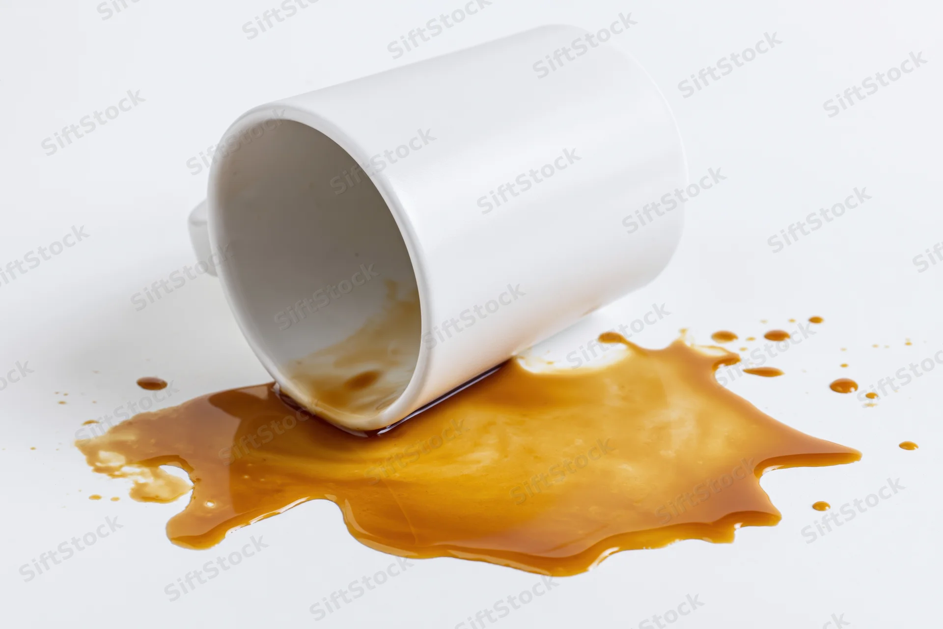 White ceramic coffee mug lying on its side with spilled coffee on a plain white surface