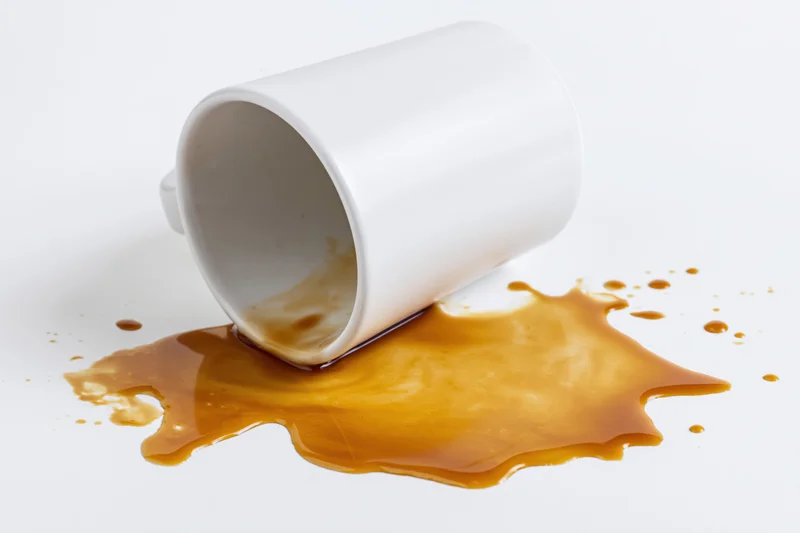 White ceramic coffee mug lying on its side with spilled coffee on a plain white surface
